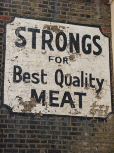 Peeling black and white hand painted sign on a building advertising Strongs Meat