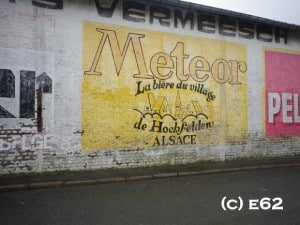 Yellow hand painted sign on a wall advertising Meteor beer