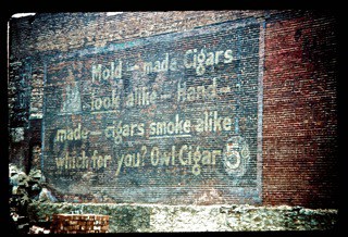 Hand painted sign on a wall advertising Owl Cigars