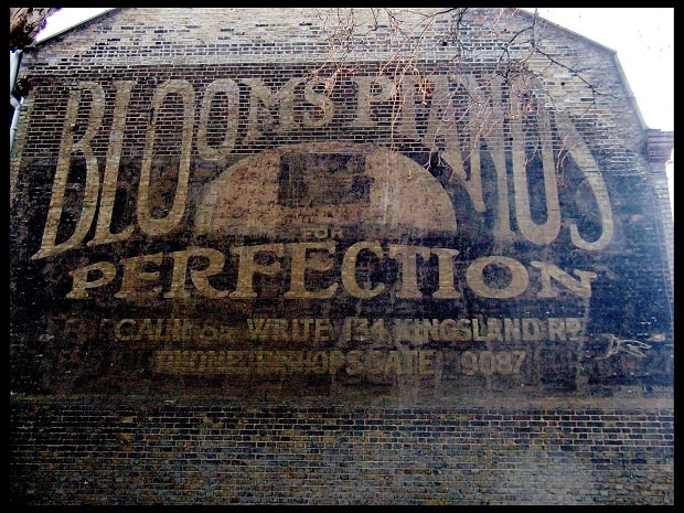 Fading hand-painted sign on a Hackney wall advertising Blooms Pianos