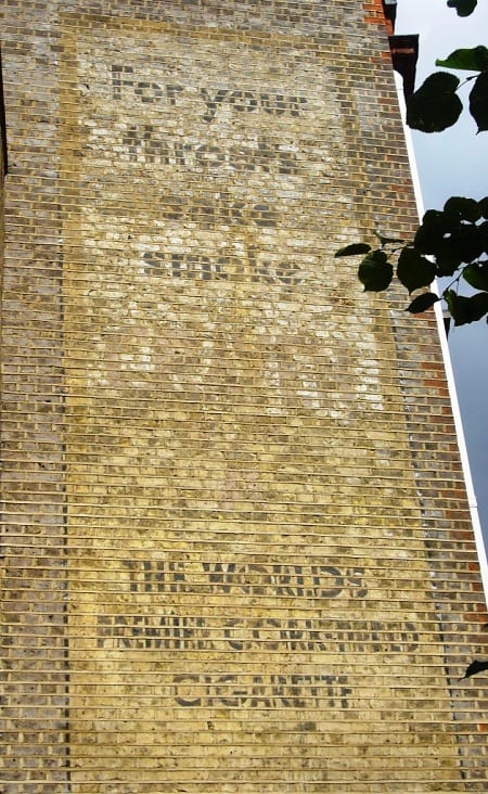 Fading painted sign on a wall (ghostsign) with the slogan 'For your throat's sake smoke'
