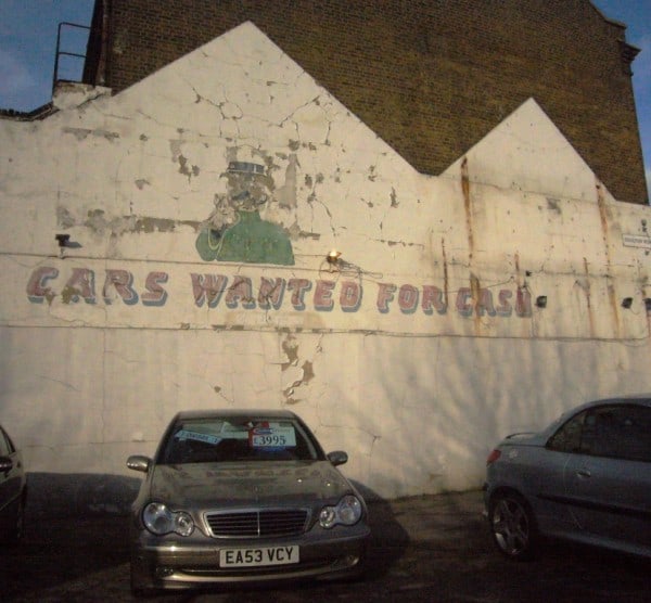 Painted sign on a wall reads 'Cars Wanted For Cash'