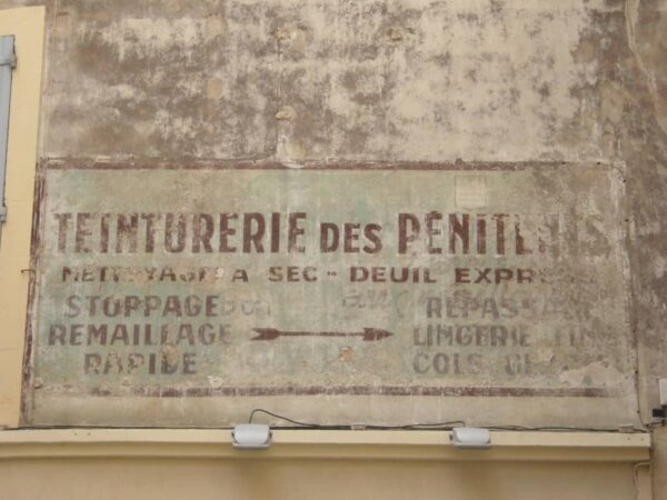 Painted sign fading on a wall advertising Teinturerie des Penitents