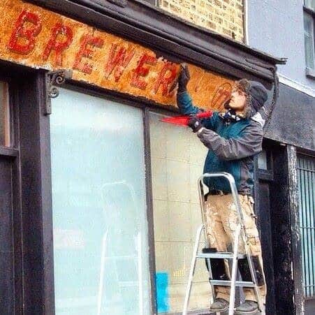 Man at work stripping back black paint to reveal a painted shop fascia