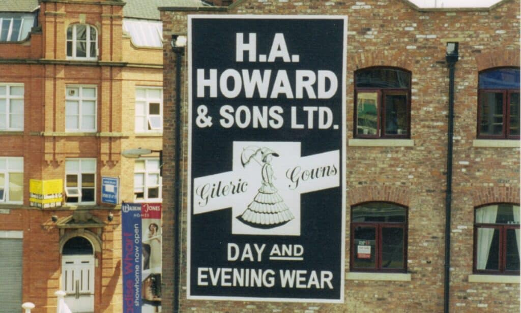 Painted sign on a wall advertising H.A. Howard & Sons Ltd, Gileric Gowns.