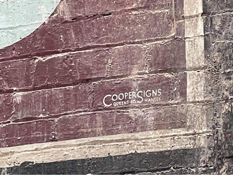 Corner of painted wall sign showing signature of signwriters Cooper Signs.