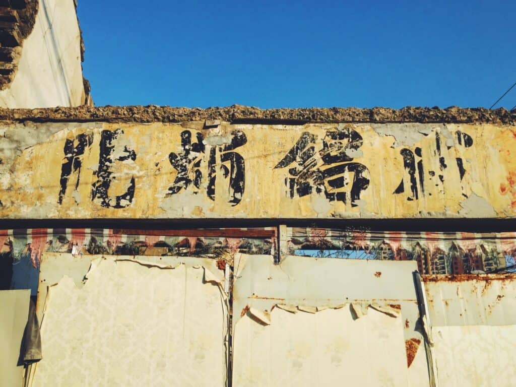 Fading painted shopfront with Chinese characters advertising a candle and cigarette shop.