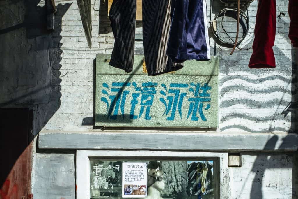 Fading painted sign with Chinese characters advertising a goggles and swimwear shop.