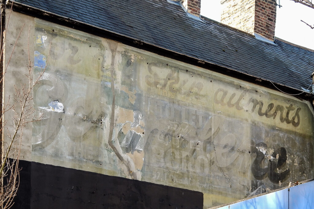 Portion of a building's wall and roof, with some barely legible letters in faded paint visible on the wall.