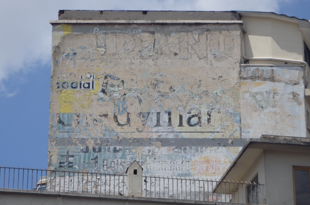 Layers of paint fading on a wall, with gimpses of lettering and pictorial work.