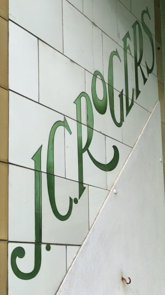 Glazed ceramic tiles with green Art Nouveau lettering on a 45 degree upwards diagonal reading "J.C. Rogers".