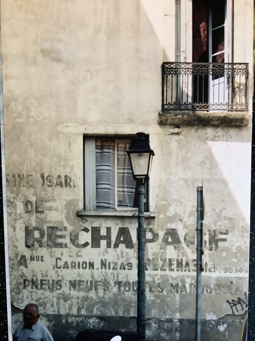Rural French townhouse building with a fading painted sign on the lower portion of the wall. The main text of this reads 'Rechapage'
