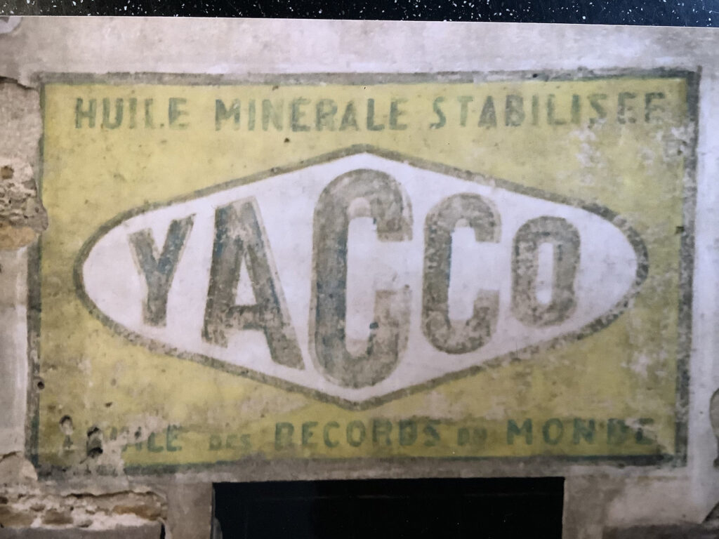 Close-up of a fading painted sign advertising a brand called 'Yacco' with it's logotype set within a horizontal diamond shape in the centre.